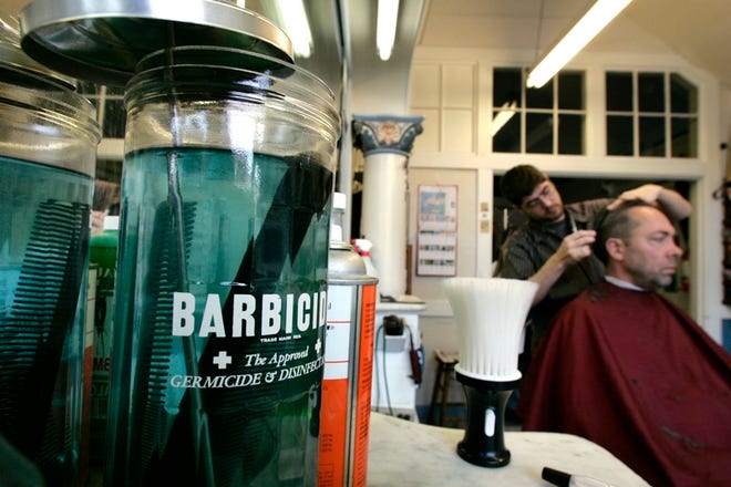 Barber Austin Harrington, left, trims the hair of Jim Swifka in the Bostonian Barber Shop in Seattle as a jar of the shop's standard Barbicide sits nearby Thursday.