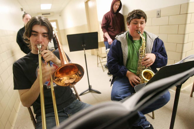 Holbrook High School students Charlie Denny, 16, clockwise from front left; Ashley Allen, 18; Tim Curtin, 18; and Eric Kenneally rehearse in a hallway at Holbrook High School recently. Music director Michelle Merrill is pushing to get funding for new instruments for students and a dedicated practice space for the band, which is sometimes forced into the hallway.
