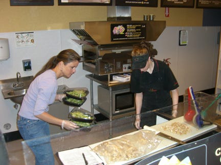 Quizno’s owner Christine Colocousis helps put salads away at the restaurant in preparation for the lunch rush.