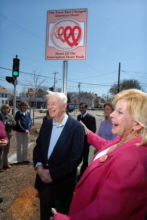 Framingham Heart Study member Walter Sullivan, 94, of Framingham stands underneath a sign marking the 60th anniversary of the study with Karen Kiley LaChance, president of the Friends of the Framingham Heart Study and a study member. The sign at the corner of Waverley and Winthrop streets was one of six put up yesterday in Framingham by the group.