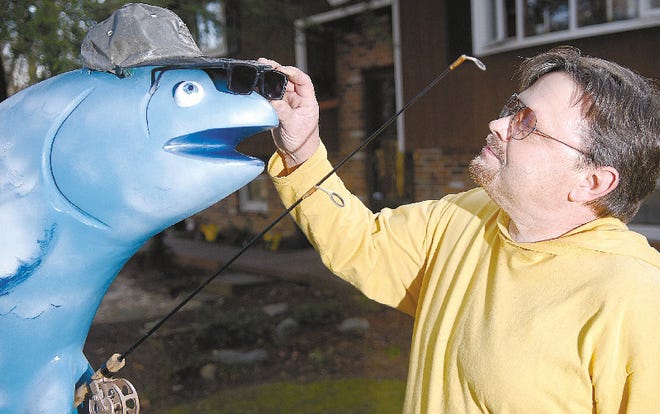 Bob Harris of Bushkill adjusts the sunglasses on a 6-foot-long trout in his front yard. Harris is one of 15 artists selected by the Monroe County Arts Council to participate in the Trout Trails and Tales project.