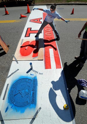 Laura LeDuc steps over wet paint while helping her father, Jacques, paint the Boston Marathon start line in Hopkinton. Jacques LeDuc, an Ashland resident, has been painting the starting line since 1981.