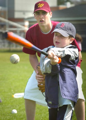 Chase Gile, 6, makes contact with the ball as John Fell, a member of the Weymouth High School varsity team, follows his swing.