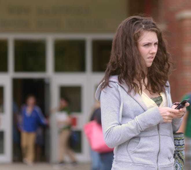 Kelsey Evans, 16, types a text message on her mobile phone Thursday outside New Hartford High School in New Hartford. Students are required to keep the phones in their lockers during school hours.
