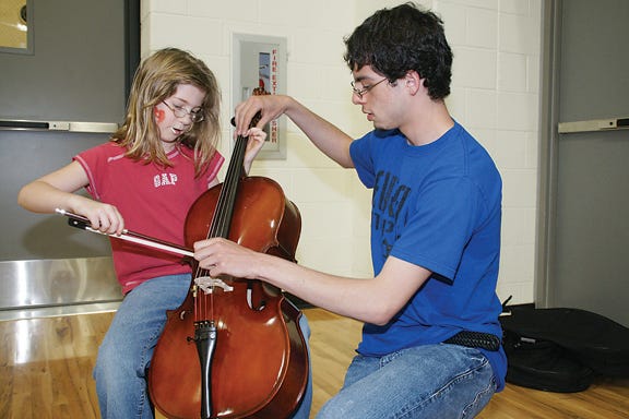 Hannah Smith, 9, of Adrian is shown how to play the cello by Calvin Howard, 16, at the Instrument Petting Zoo during the Fine Arts Festival at Adrian High School on Saturday.