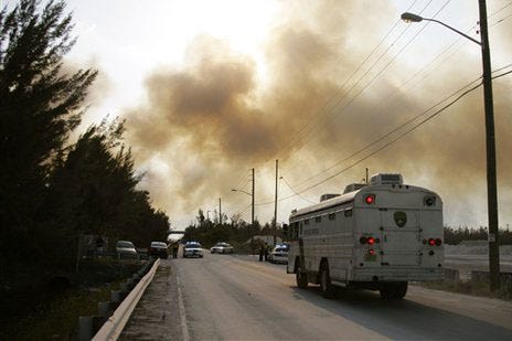 A prison bus approaches a road block leading to the Metro West Detention Center in Miami Monday, April 28,2008 as a wild fire nears the prison and heavy smoke hangs overhead. Prison officials are moving the 2,634 inmates at the center.
