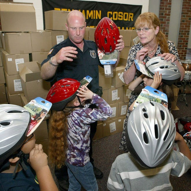 Police Officer Jason Berger and Gail Lamb-Doto give out bicycle helmets Friday to kindergartners at Benjamin Cosor Elementary School in Fallsburg.