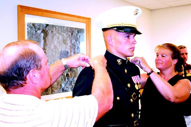Dan and Patti apply the epaulets of an officer to their son's uniform.