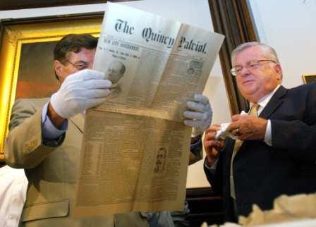 City Councillor Dan Raymondi and City Clerk Joseph Shea look at a copy of The Quincy Patriot newspaper from June 16, 1896, that was placed in a time capsule for the dedication of the Abigail Adams Cairn.