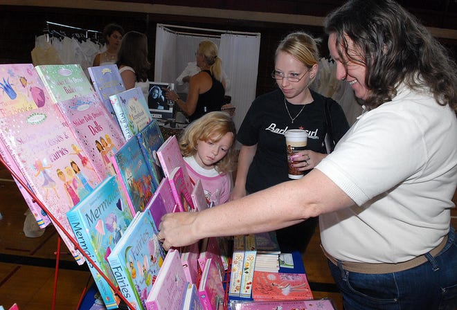 Janet Luchies, right, shows Barbara Louks of Fennville and her eight-year-old daughter Rebecca a selection of Usborne children's books during the Royal Extravaganza Women's Expo Saturday at the Holland Civic Center.