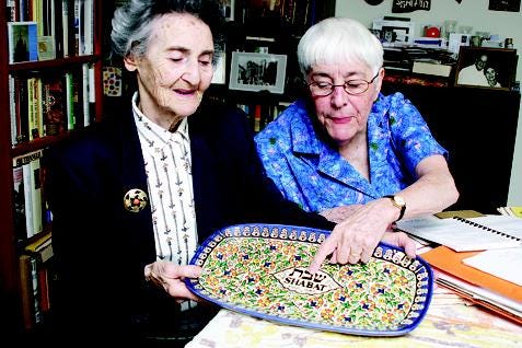 Mira Kimmelman, left, and Eileen Handler look at a special Shabat plate, while reminiscing about the years spent cooking together for the Jewish Sisterhood Food Fair.