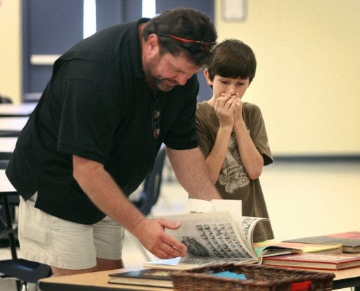 Brandon Fuqua, 10, gasps after his father Rusty shows him an action shot of his mother jumping as a cheerleader from a 1979 year book at Vanguard High School.
