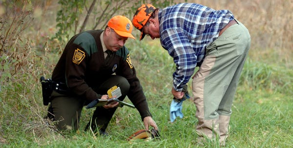 Officer Eric Stafirny, of the Pennsylvania Game Commission, left, confiscates the shotgun used by the hunter, right, near the scene of the shooting near Dingmans Ferry on Saturday afternoon.