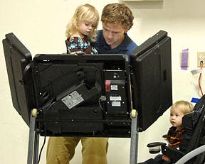 Mark Hodge holds his daughter Hayden, 3, while his sons Brady, 1, and Brewer, 9 months, wait as he votes at the Knights of Columbus Hall on north Stadium Boulevard.