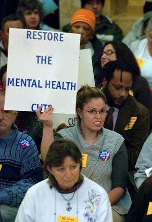 Danielle Zdenek of Ashland, unit coordinator of Elliot House of Needham, holds a sign during a protest of mental health cuts at the State House in Boston on Tuesday. Mental health workers and program participants talked about the effects of the cuts on their programs and delivered a petition to the governor's office.
