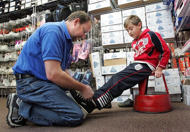 Mike Leivi, owner of Play It Again Sports in Dedham, helps Justin Plakias, 8, of Medfield try on hockey skates.