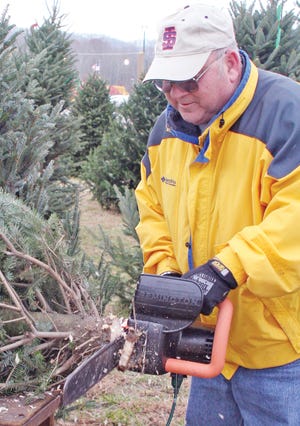 Dale Allen trims a tree at the Christmas tree lot next to TnBank off of its Manhattan Avenue entrance.