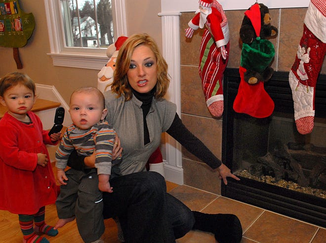Petrina Oldfield points to a broken piece of framing on a gas fireplace that leaked carbon monoxide at her 2 Lydia Lane home in Milford. She holds 5-month-old Austin while 20-month-old Venecia stands neaby.