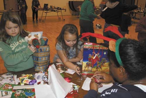 Second graders Jenna Conley and Samantha Lacky watch as volunteer Connie Glover wraps the gifts they’ve chosen at the Bazaar.