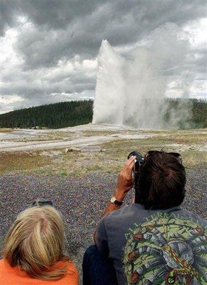 In this Friday, Aug. 15, 1997 file photo, an unidentified pair of visitors to the Yellowstone National Park photograph the Old Faithful geyser as it rockets 100-feet skyward , in Wyoming. Hundreds of small earthquakes at Yellowstone National Park in recent weeks have been an unsettling reminder for some people that underneath the park's famous geysers and majestic scenery lurks one of the world's biggest volcanoes.