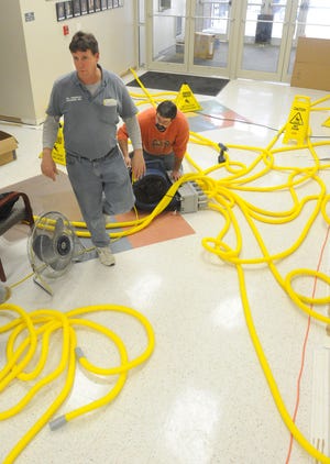 Barry Lasco, left, owner of All American Cleaning, walks through the front area of Tri-County Christian School where supervisor Dennis Metz sets up a blower that will dry inside the walls of the school Monday. Water covered a large portion of the school after a pipe broke Friday night.