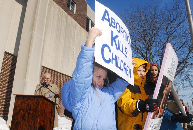 Hadassah Ortega, 7, of Freeport holds a sign with others while Msgr. P. William McDonnell of St. Thomas Aquinas Church speaks during a prayer service hosted by Stephenson County Right to Life outside the Stephenson County Courthouse on Thursday, Jan. 22, 2009.