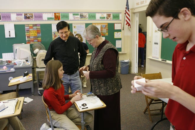 Rev. Howard Ziemba watches Sister Barbara Klodt as she helps Emily Otto seated, and Eddie Reeves make corporal works of mercy boxes during an eighth grade class at Sacred Heart of Mary Elementary School that will close at the end of this school year.