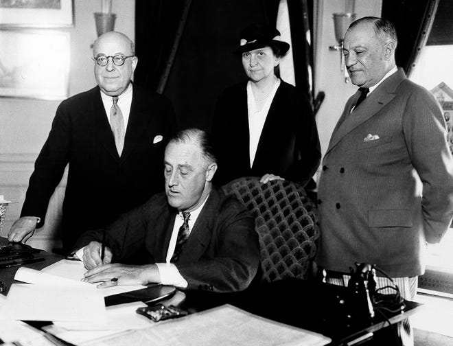 In a 1933 file photo, President Franklin D. Roosevelt is shown signing the Wagner Unemployment Bill at the White House in Washington. Standing, from left are: Rep. Theodore A. Peyser, Secretary of Labor Frances Perkins, and Sen. Robert Wagner.