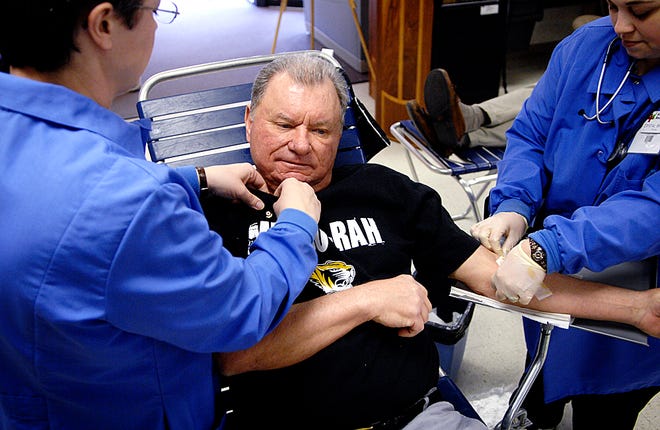 Susan Leach, left, puts a pin of recognition on Stan Grebing’s shirt Friday as Crystal Brandy puts a bandage on his arm after he gave his 200th unit of blood at the American Red Cross Donor Center, 1511 S. Providence Road.