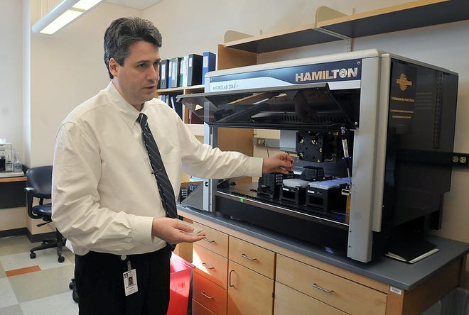 Researcher John Landers of Framingham explains the function of the robotic DNA "liquid handler" at the Lazare Research Lab in Worcester on Friday. The machine is able to fill test capsules quickly and safely for thei ALS research.
