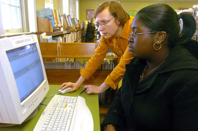Library worker Rima Tamule helps Johanna Paterson, 15, of Brockton, with a computer at the west branch of the Brockton Library. Hours at the branch have been severely curtailed from 40 to 15.