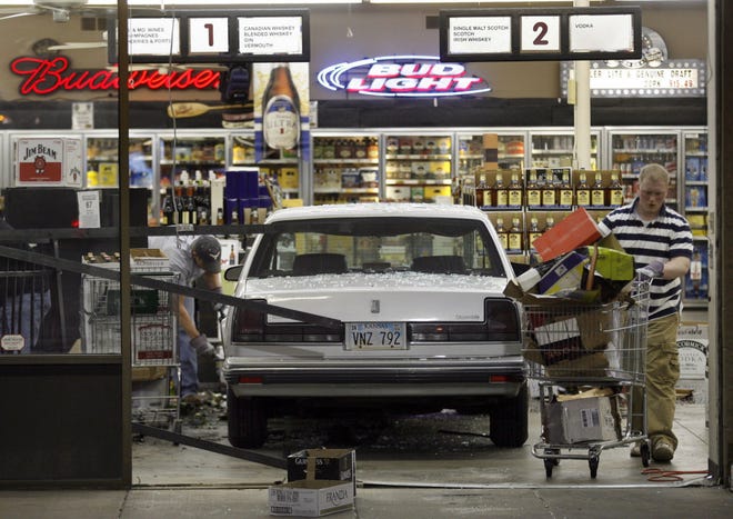 A white Oldsmobile finds itself between Evan Williams bourbon on aisle 1 and Lord Calvert whiskey on aisle 2 on Monday night at Devlin's Wine and Spirits, S.W. 29th and Wanamaker. Employees clean up the mess caused by the car. Topeka police Capt. James Scott says the driver was a woman, and alcohol was a contributing factor in the accident.