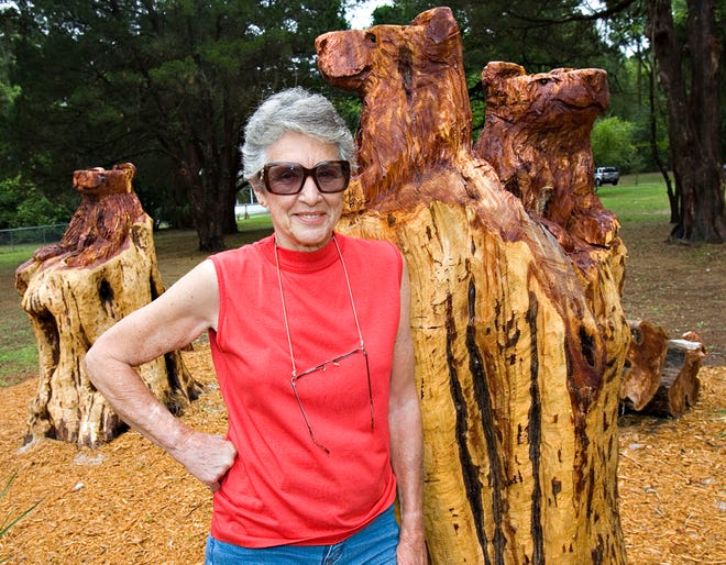 Elaine Conover poses next to two of her cedar trees that she had cut down and then had the stumps carved into a family of bears in her front yard.