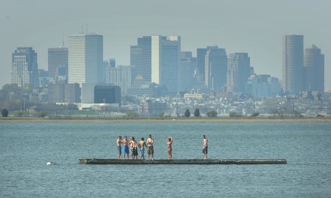 Boston fills the background as young people take to a floating dock in Quincy Bay on Tuesday. People flocked to the water to cool off on a day when temperatures rose to around 90.