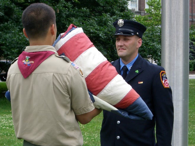 New York City firefighter Jim Sands accepts the folded flag from a member of Boy Scout Troop 42. The New York Says Thank You National 9/11 Flag Tour kicked off in Quincy, and will end at the Little Sioux Boy Scout Camp in western Iowa.