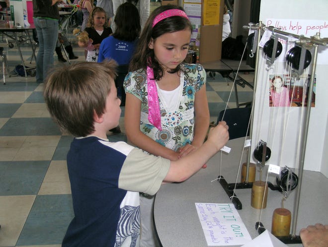 Calliope Tarsi, 7, looks on as Brandon Siscoe, 5, tries her science expo project about pulleys.