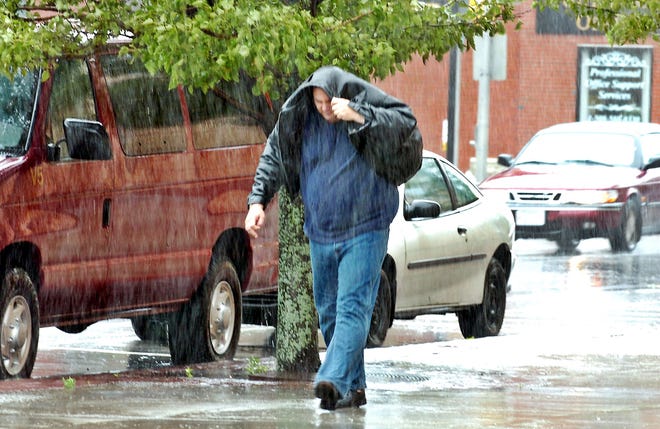 A pedestrian shields himself from heavy rain on Main Street in Brockton on Monday.