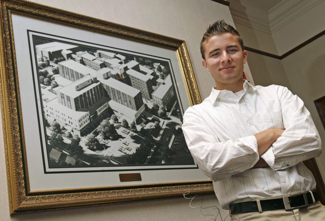 Ethan Steigert, a Malone University graduate, has been offered a job as a management trainee at Aultman Foundation. Behind him is a photo of Aultman Hospital.