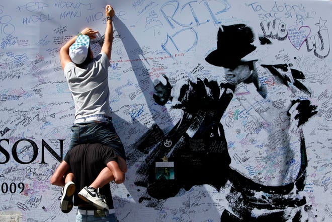 Luis Benguria of Spain sits on the shoulders of Pedro Vicente, also of Spain, as he signs a large poster at the Staples Center in Los Angeles, Calif., Sunday, July 5, 2009. The venue is the planned location for late pop star Michael Jackson's memorial service scheduled for Tuesday, July 7.