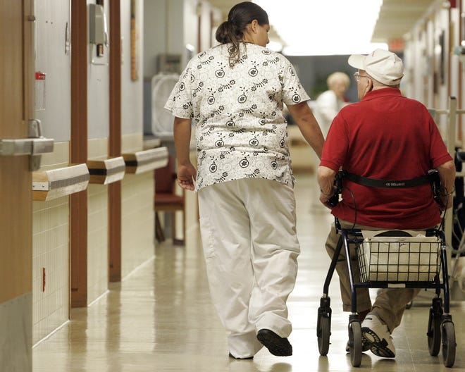 Certified Nursing Assistant Griselda Mendoza (left) walks John Sanden down a hallway Tuesday, July 7, 2009, at River Bluff Nursing Home in Rockford.