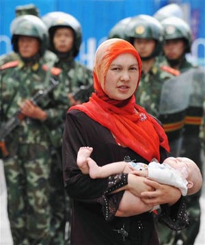 Uighur woman with a child walks past paramilitary police on patrol near mosques in Urumqi, western China's Xinjiang province, Friday, July 10, 2009. Boisterous crowds turned up at mosques in this riot-hit western China city despite announcements that Friday prayers were canceled due to the recent ethnic violence and forced officials to let them in.