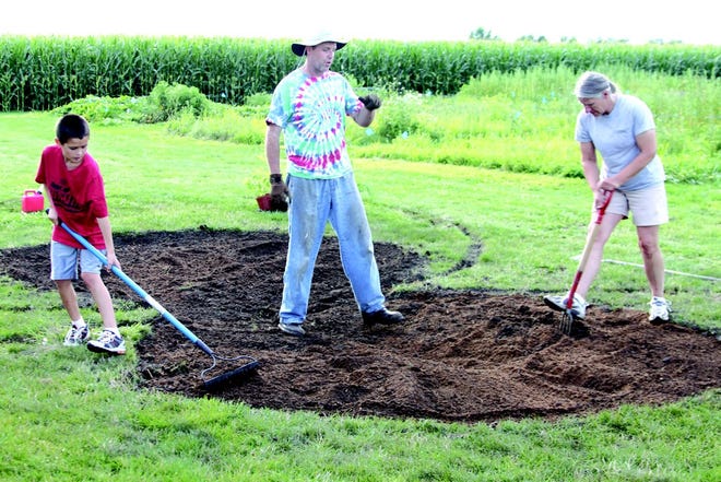 (Center) Monmouth College Professor Bradley Sturgeon, his son, Zach, 10, and Kathy Hale-Johnson prepare the soil for planting a rain garden Monday night at the New River of Life Church.