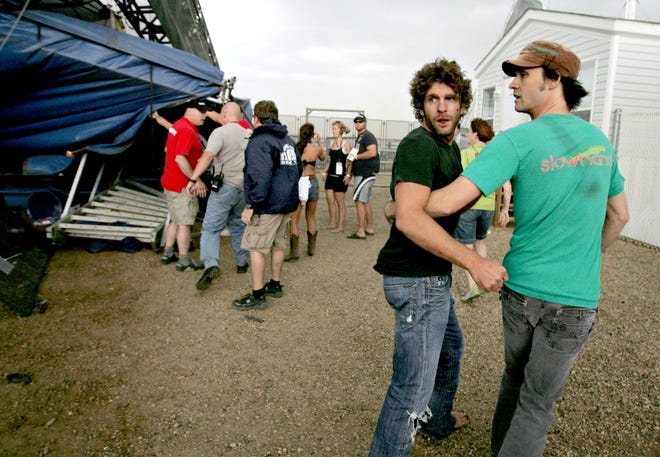 Singer Billy Currington, center, is escorted away from the stage after it flipped in a storm Saturday during the Big Valley Jamboree in Canrose, Alberta. Strong winds and heavy rain began hitting the Big Valley Jamboree in Camrose, east of Edmonton, around 6 p.m., said Camrose Police Chief Darrell Kambeitz. He confirmed one death and said all 15 injured were taken to hospitals. (AP Photo/The Canadian Press - Amber Bracken, Edmonton Sun)