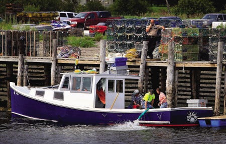 Water is pumped out of a boat owned by lobsterman Keith Simmons on Wednesday as a Knox County sheriff looks on in Owls Head, Maine. Officials are investigating an act of vandalism Tuesday night in the harbor that left two lobster boats sunk and a third almost underwater.
