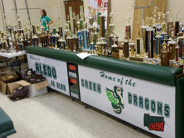 This table is holding trophies that are for sale at the Apollo Elementary gymnasium sale, for $1 apiece. The table is a silent auction item.