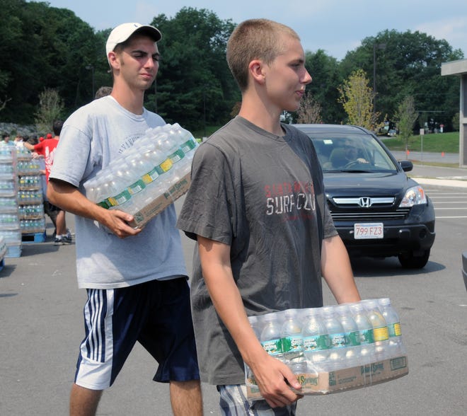 From left, brothers Christian, 18, and Elijah, 15, Trepanier earn $10 an hour loading water into vehicles at Milford High School.