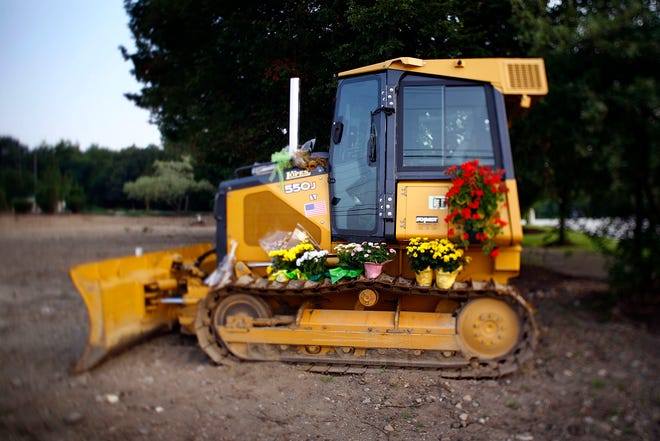 The bulldozer that Manny Lopes used to help create a memorial park in Marshfield sits on the site, decorated with flowers. Lopes died of a heart attack last week, not long after he finished his volunteer work on the park project.