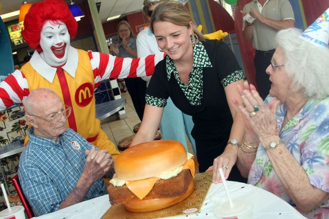 MAGGIE FITZROY/StaffMcDonald's representative Megan Denk presents Harold and Lillian Bergman with a cake shaped like a giant fish filet sandwich Wednesday during a celebration in honor of Harold Bergman's 106th birthday.