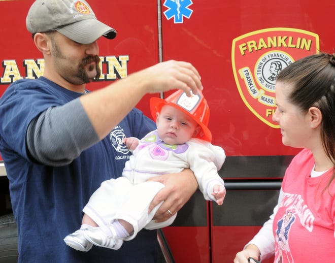 Franklin firefighter Victor DaCosta places a fire hat on his 4-month-old daughter, Avery, as his wife, Christie, looks on during the King Street fire station open house.