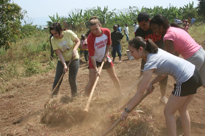Hudson High School students visiting Rwanda as part of an exchange program work with Rwandan students to clear land that will be used for a youth center.